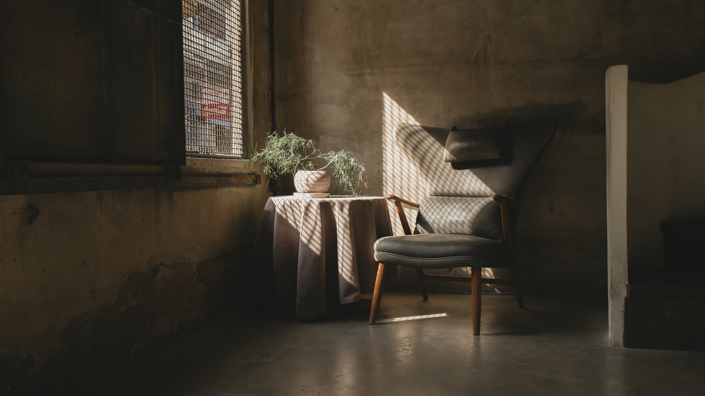An empty armchair beside a window in quiet, low light